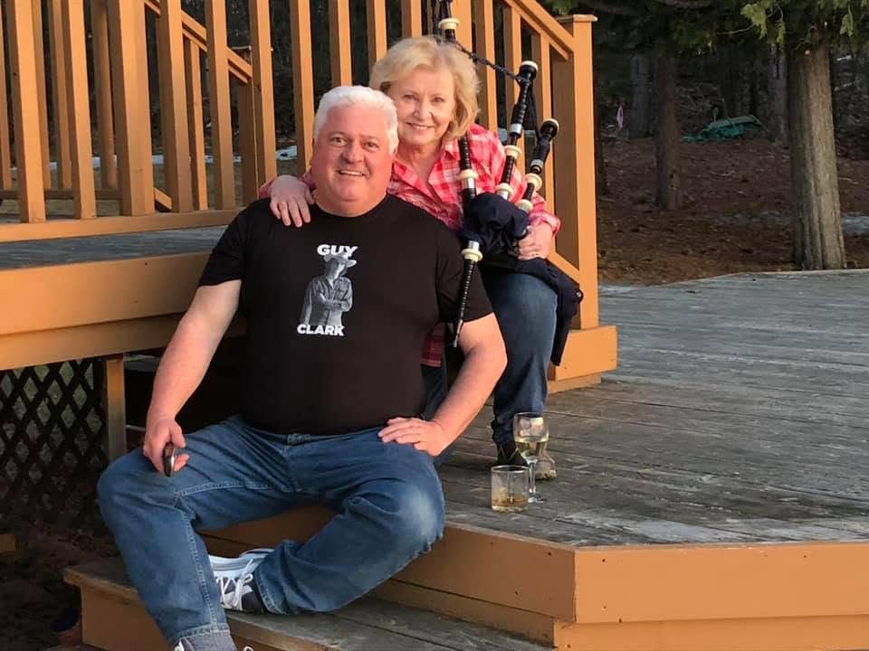 Ron in a Guy Clark shirt on the deck steps, Annadeane with her bagpipes behind him