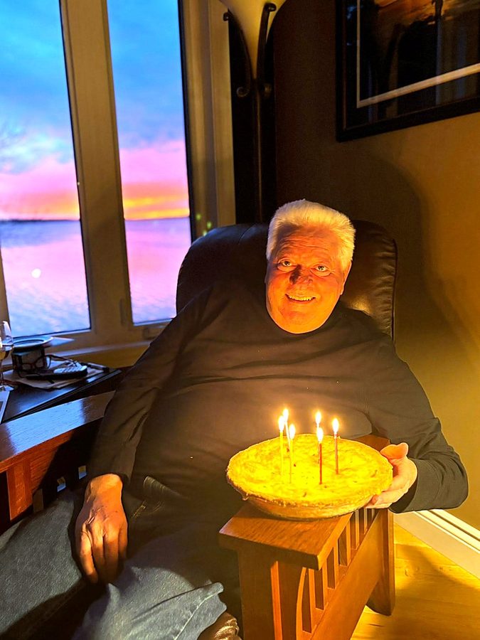 Ron with a birthday pie and candles, sunset over the lake behind him
