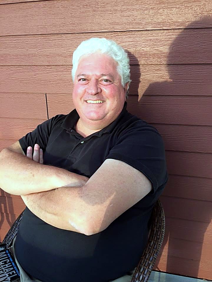 Ron smiling with his arms crossed, evening light, against red board siding