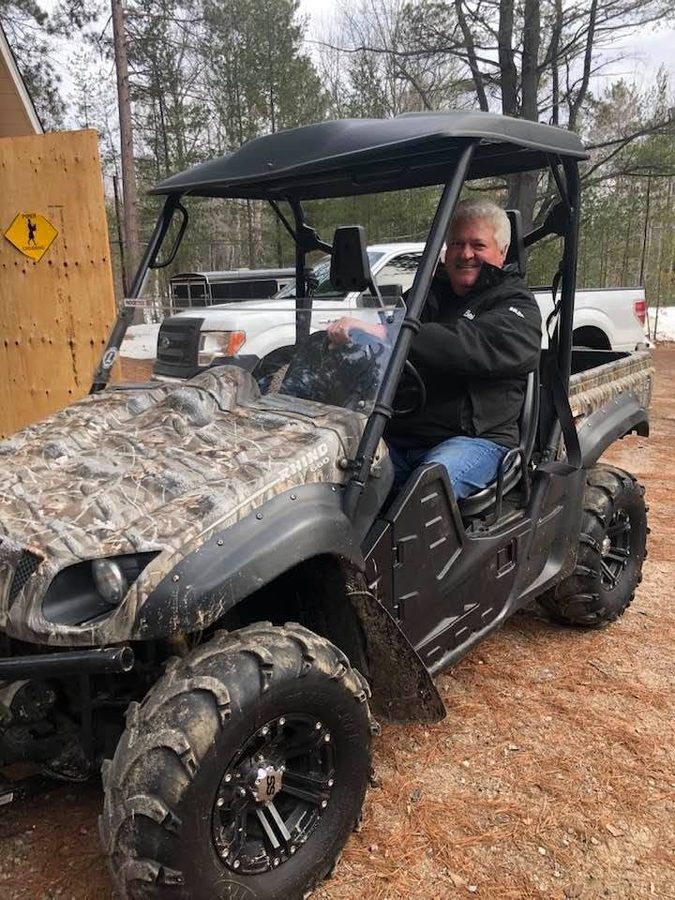 Ron at the wheel of a side-by-side at a camp in the bush, snow on the ground
