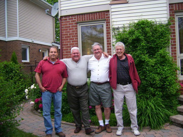 Ron with three men, arms around each other, outside a house