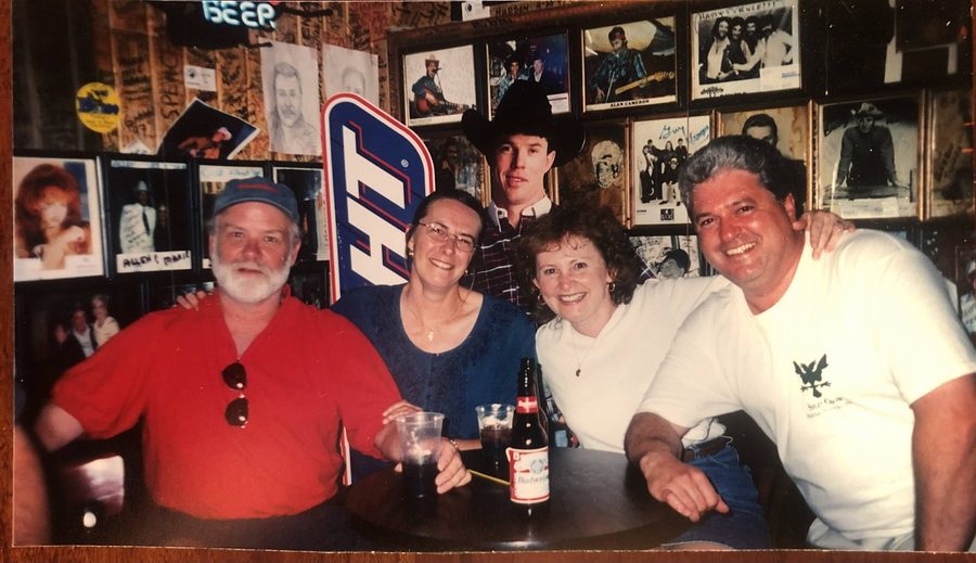 A younger Ron at a bar table with four others, framed country music photographs behind them