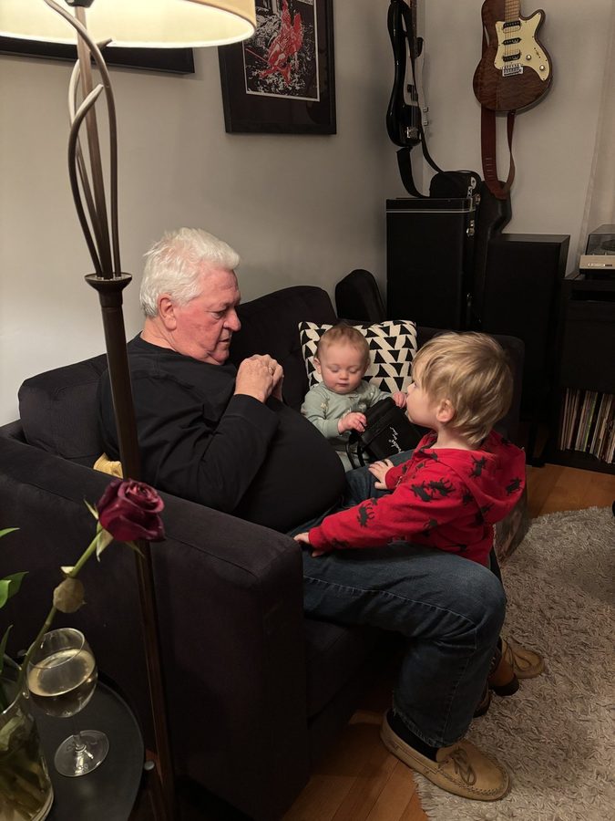 Ron on the couch with his grandsons, the baby tucked in beside him, the older one climbing onto his lap